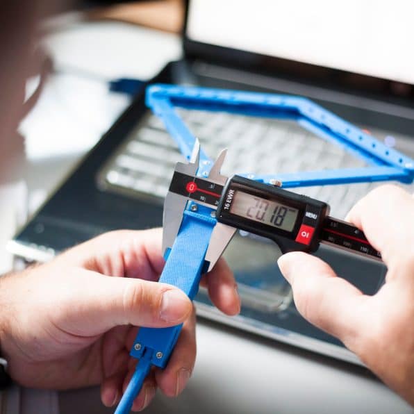 Precision Measurement of a Prototype. Engineer's hands using an electronic caliper to check a component printed with a 3D printer. Focus on technology and innovation.